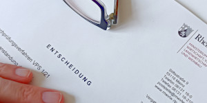 Finger und eine Brille liegen auf einem Blatt Papier, welches den Schriftzug Entscheidung trägt.