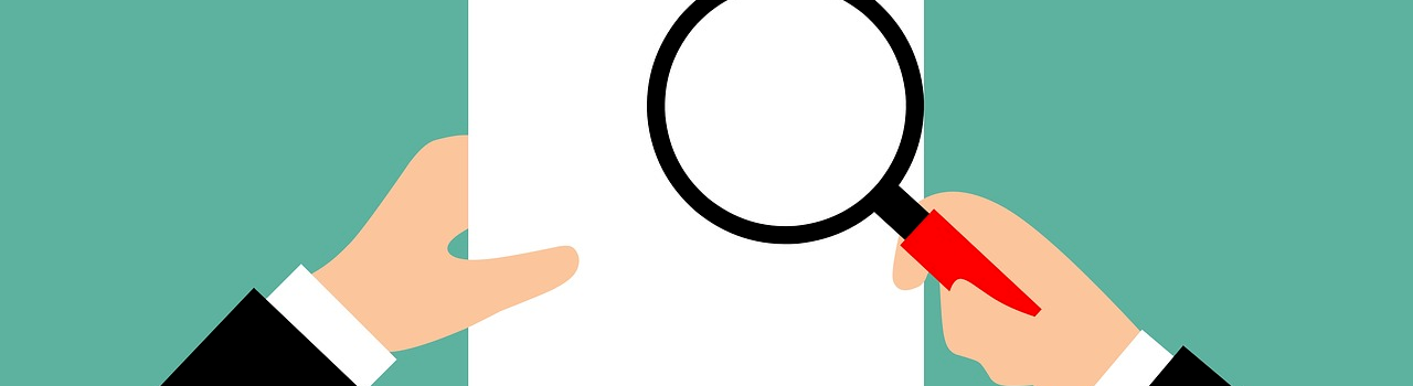 Linke Hand hält ein weißes Blatt Papier. Rechte Hand hält eine Lupe über dem Papier.